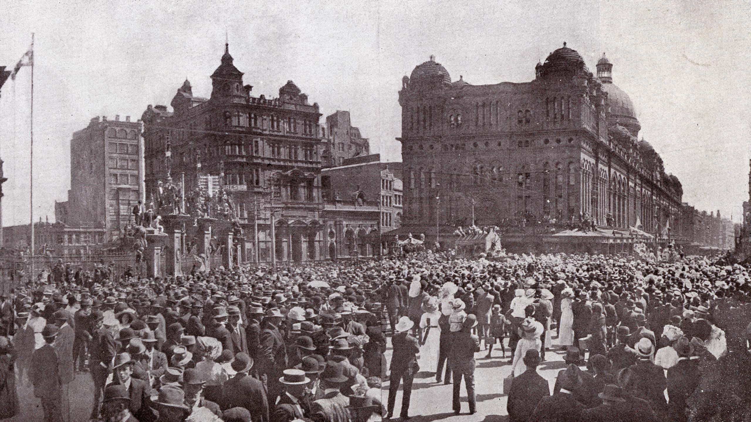 A crowd in suits and women wearing bonnets fill George Street near Town Hall.