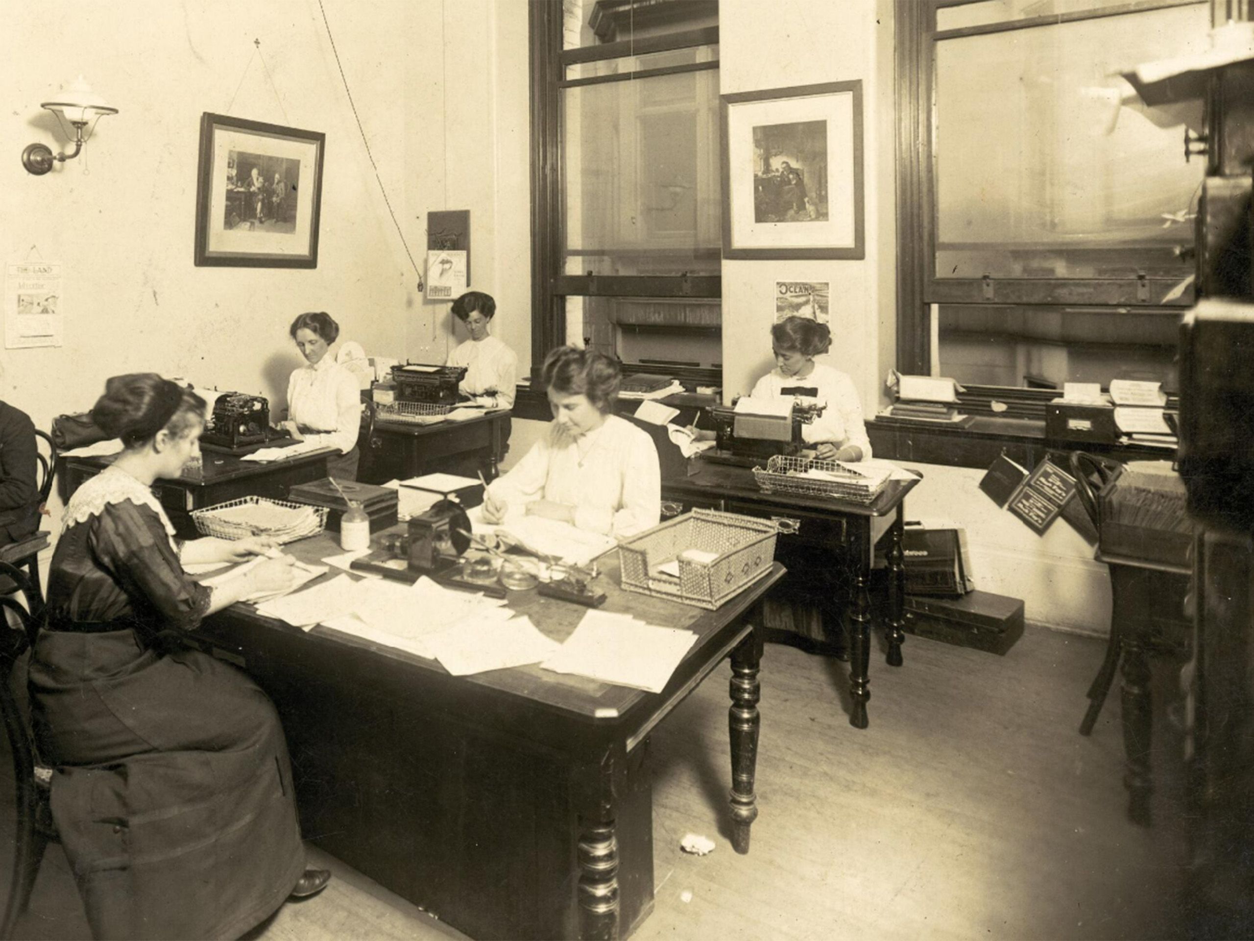 Employees sitting at desks in a room, with papers and typewriters.
